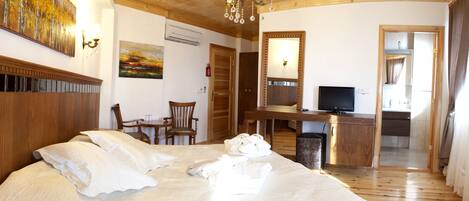 A hotel room with a large bed, a desk with a TV, a chair, a small table, and a painting on the wall.