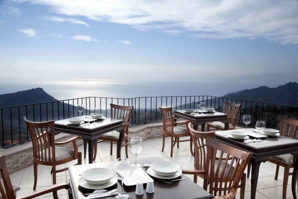 Une terrasse avec des tables dressées pour le dîner, offrant une vue sur un paysage montagneux.