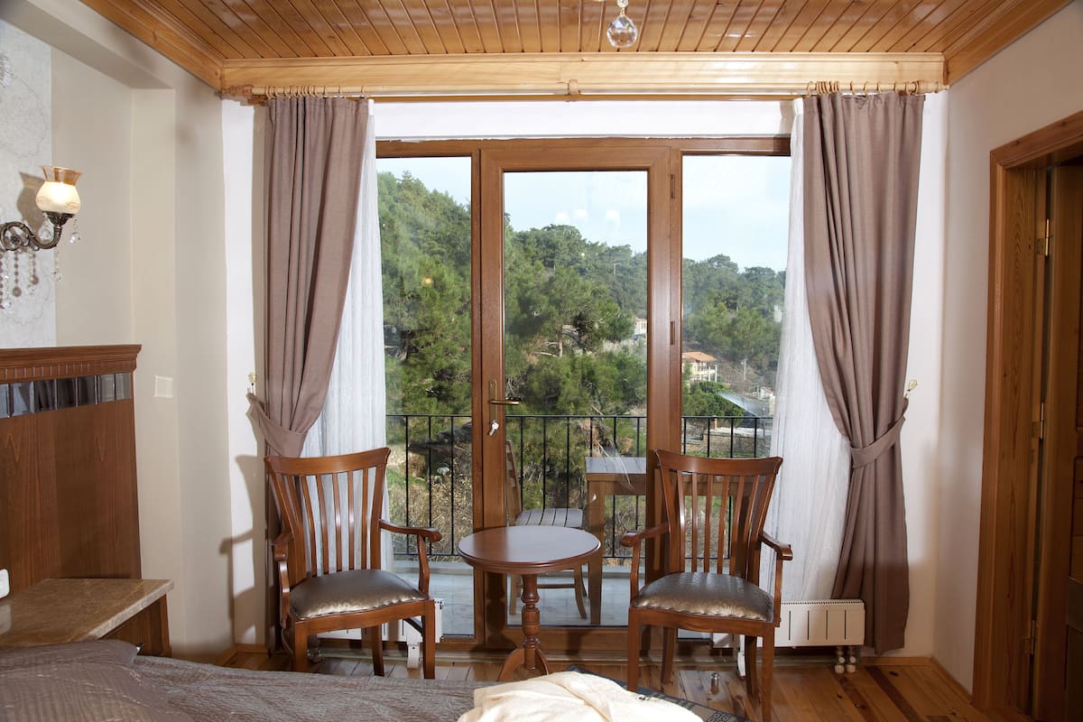 Une pièce avec un plafond en bois, un lit, une petite table avec des chaises et une vue sur un paysage montagneux, visible à travers de grandes fenêtres.