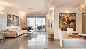 Uma sala de estar moderna com sofá, mesa de centro e área de jantar. Há uma janela grande com vista para a cidade.