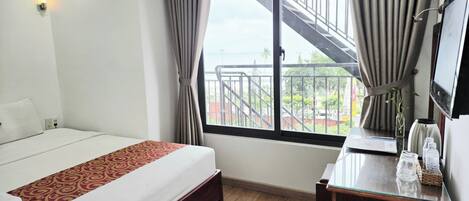 A hotel room with a bed, a desk, a mirror, and a window with a view of a balcony and outside scenery.