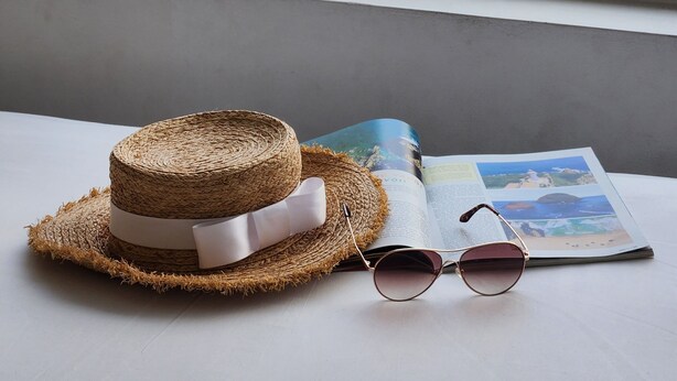 A straw hat, sunglasses, and an open magazine on a table by a window with a view of the beach. - Le Soleil Hotel Nha Trang (Nha Trang)