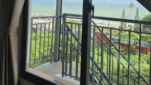 A room with a large window overlooking a balcony with a view of a beach and palm trees. - Le Soleil Hotel Nha Trang (Nha Trang)