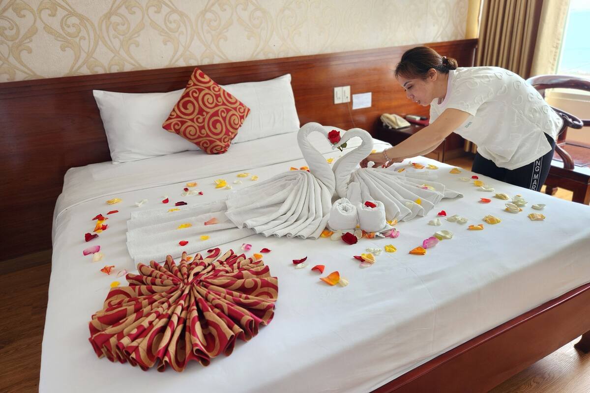 Een opgemaakt bed met een zwaan van handdoeken, een waaier van rode en beige handdoeken, en losse bloemblaadjes.