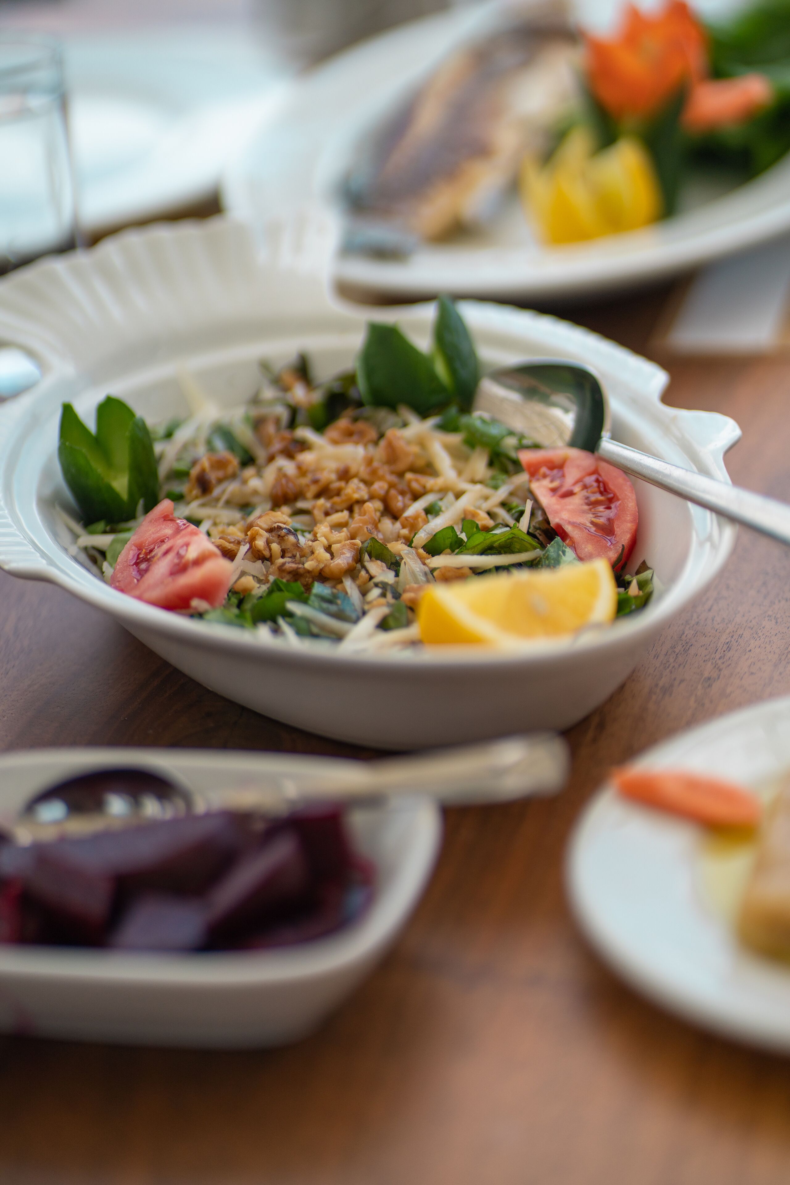 Une table à manger avec une assiette blanche contenant une salade, une fourchette et une cuillère.