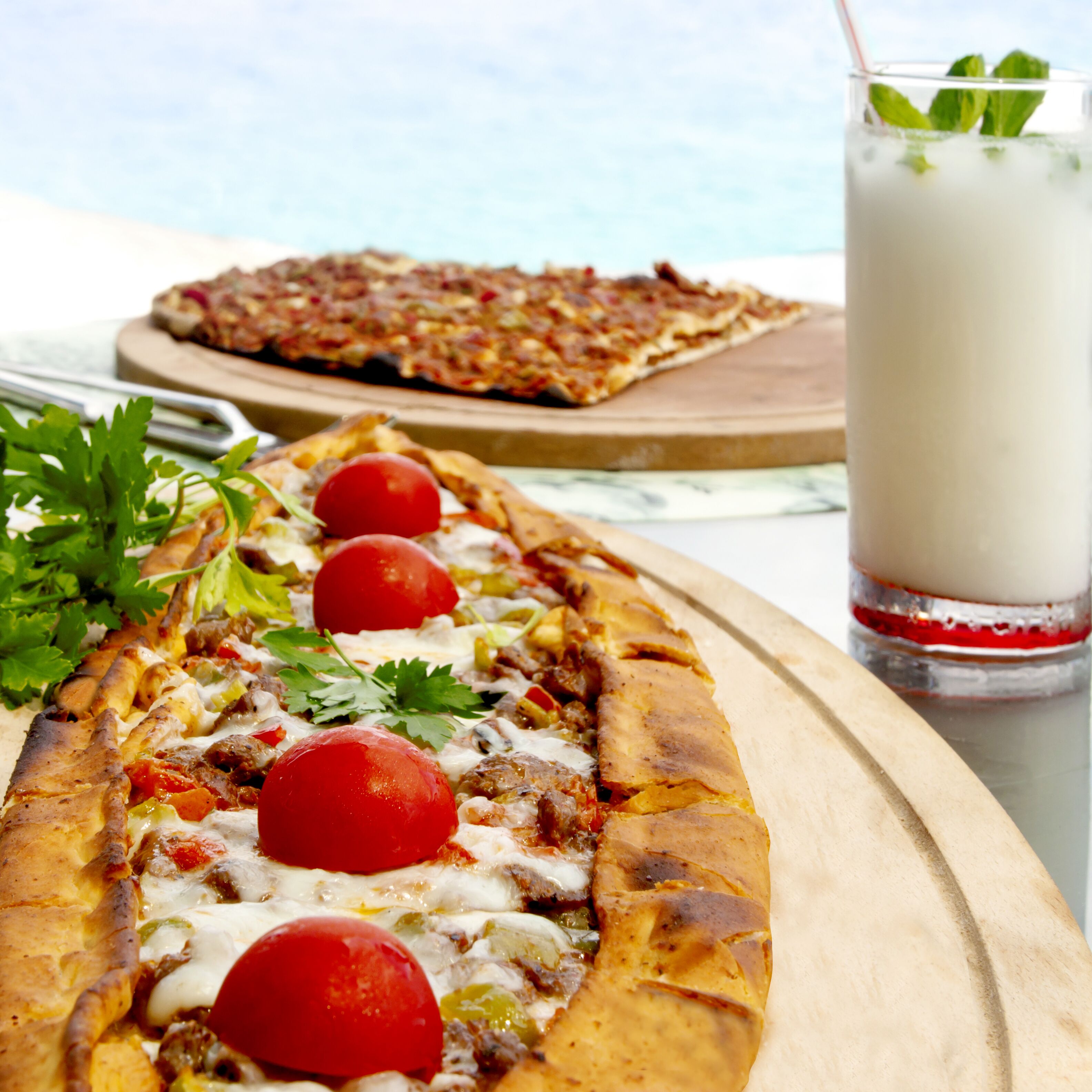Una barra de pan con ingredientes, un vaso de bebida y una pizza sobre una tabla de madera.