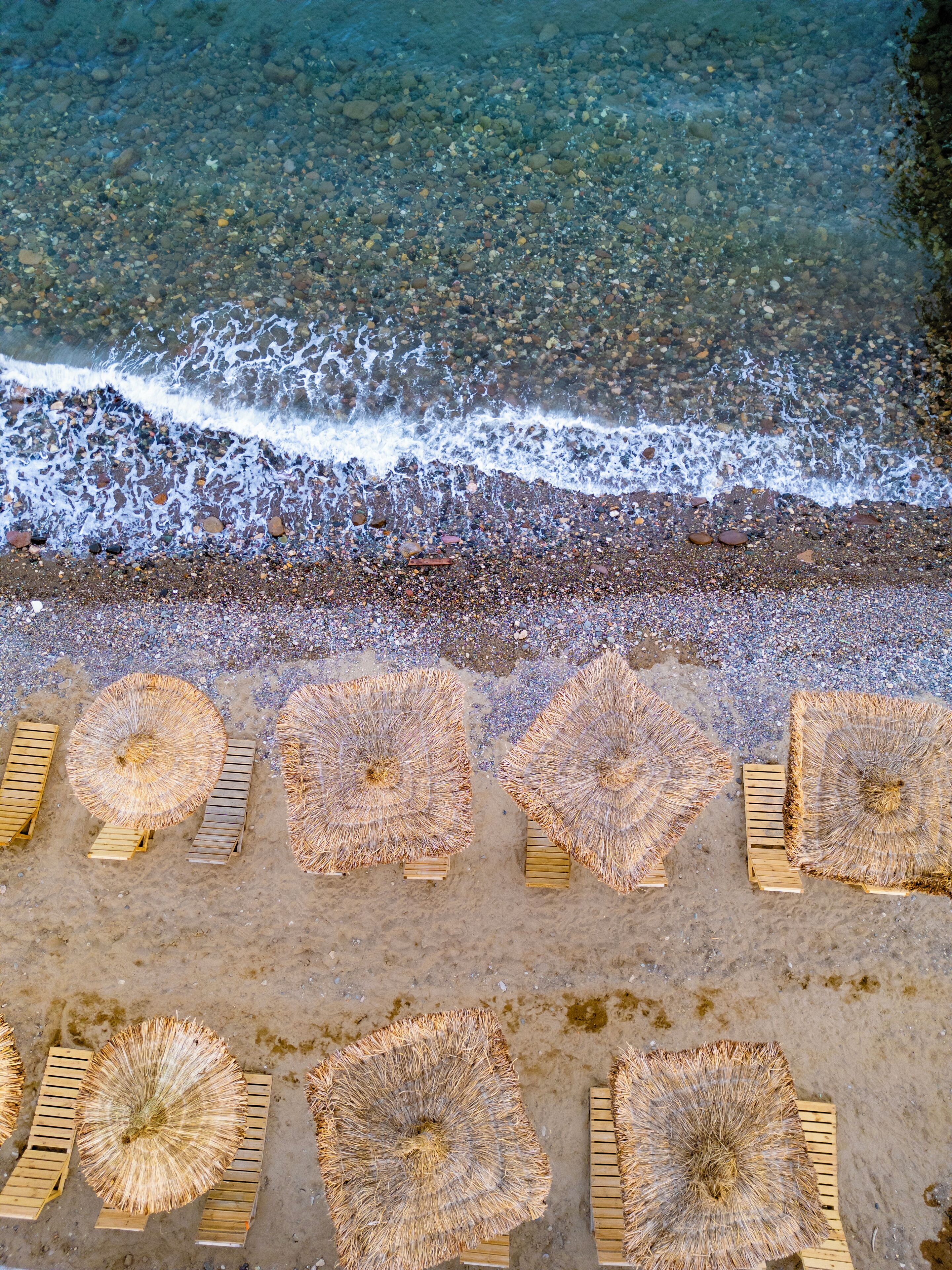A beach with umbrellas and wooden loungers arranged on the sand.