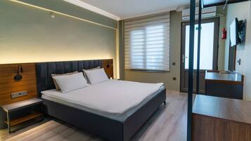 A modern bedroom with a large bed, bedside tables, a built-in bench, a mirror, and a window with blinds.