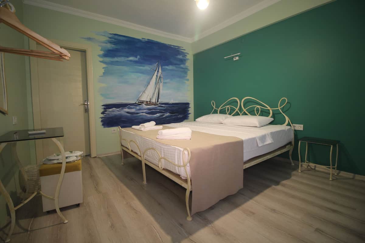 A bedroom with a bed, a painting of a sailboat, a small table, and a chair.