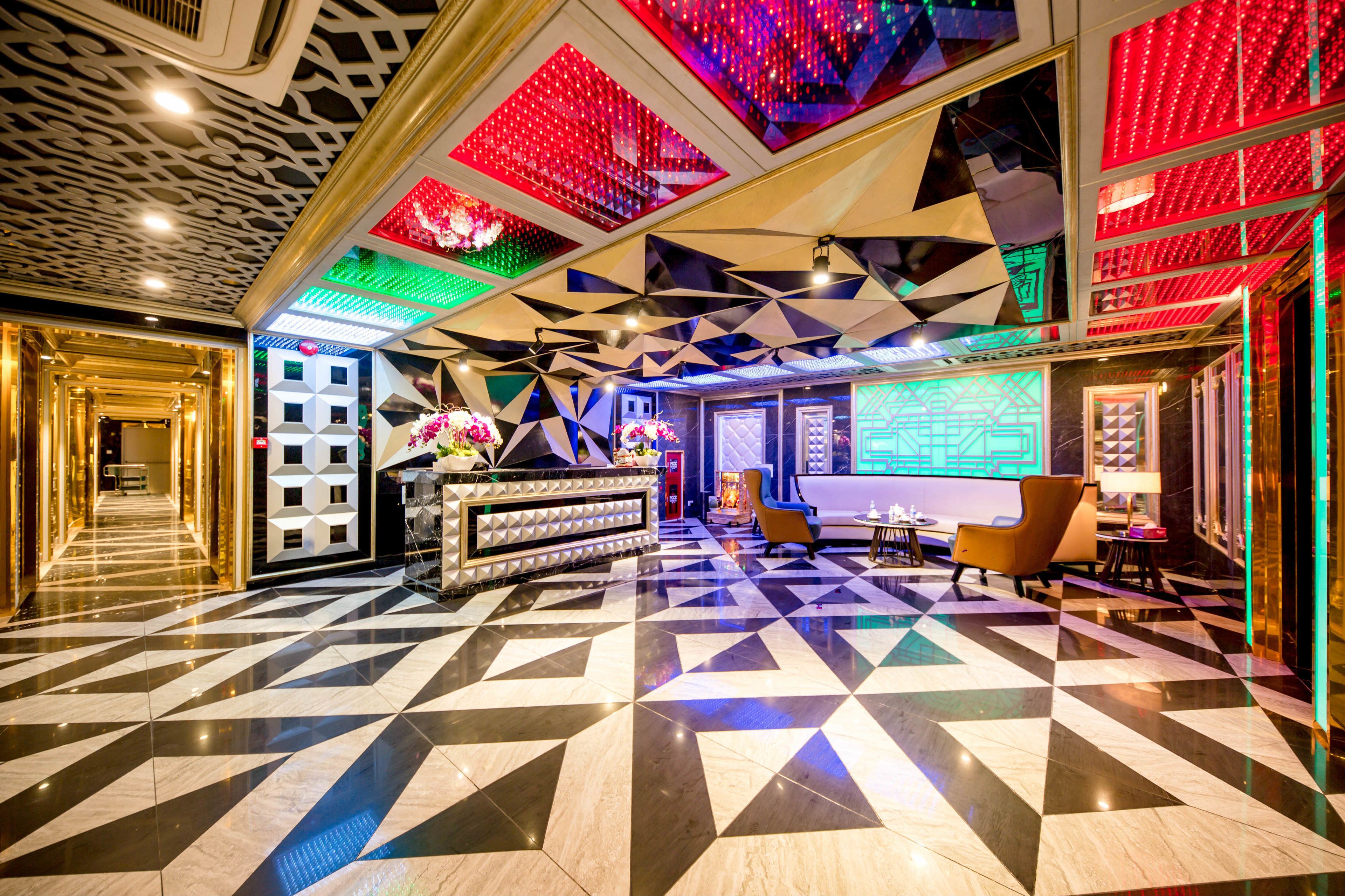 A lobby with a geometric patterned floor, a reception desk, and a seating area with chairs and tables.