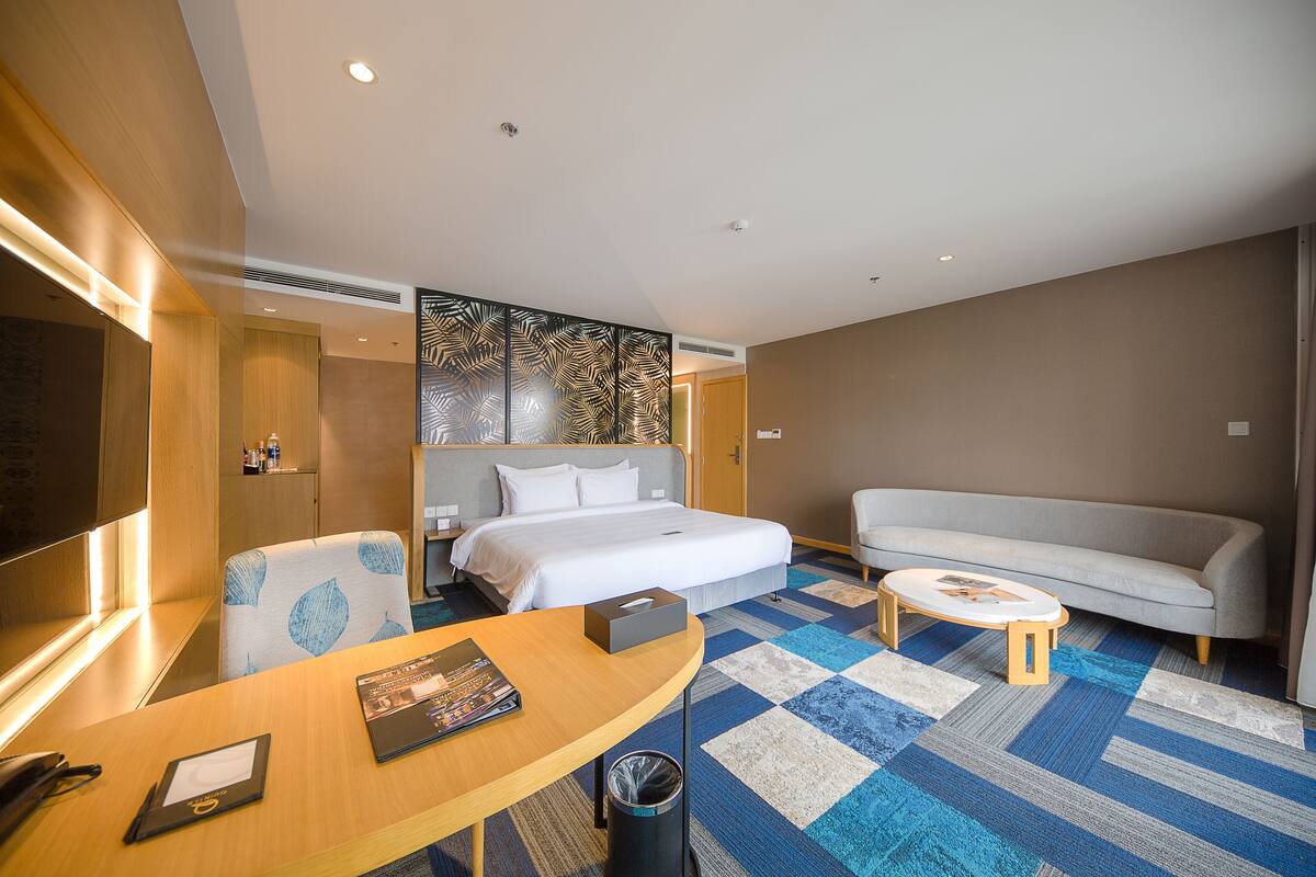 Quarto de hotel com uma cama, um sofá, uma escrivaninha e um cesto de lixo.