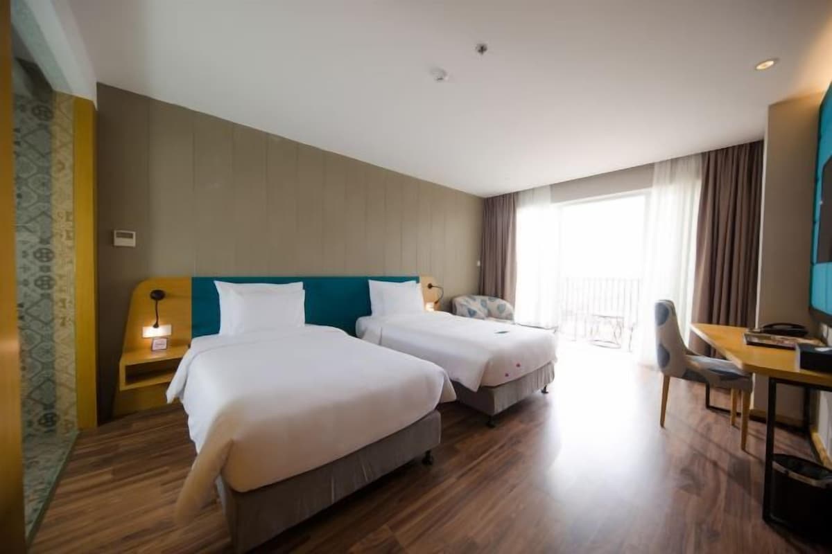 Habitación de hotel con dos camas, un escritorio, una silla y un ventanal grande.