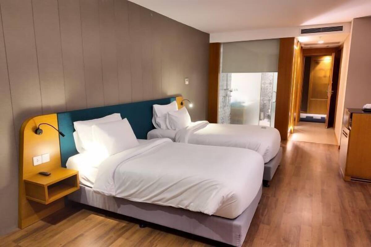 Quarto de hotel com duas camas, uma mesa de cabeceira, uma escrivaninha e vista para o exterior.