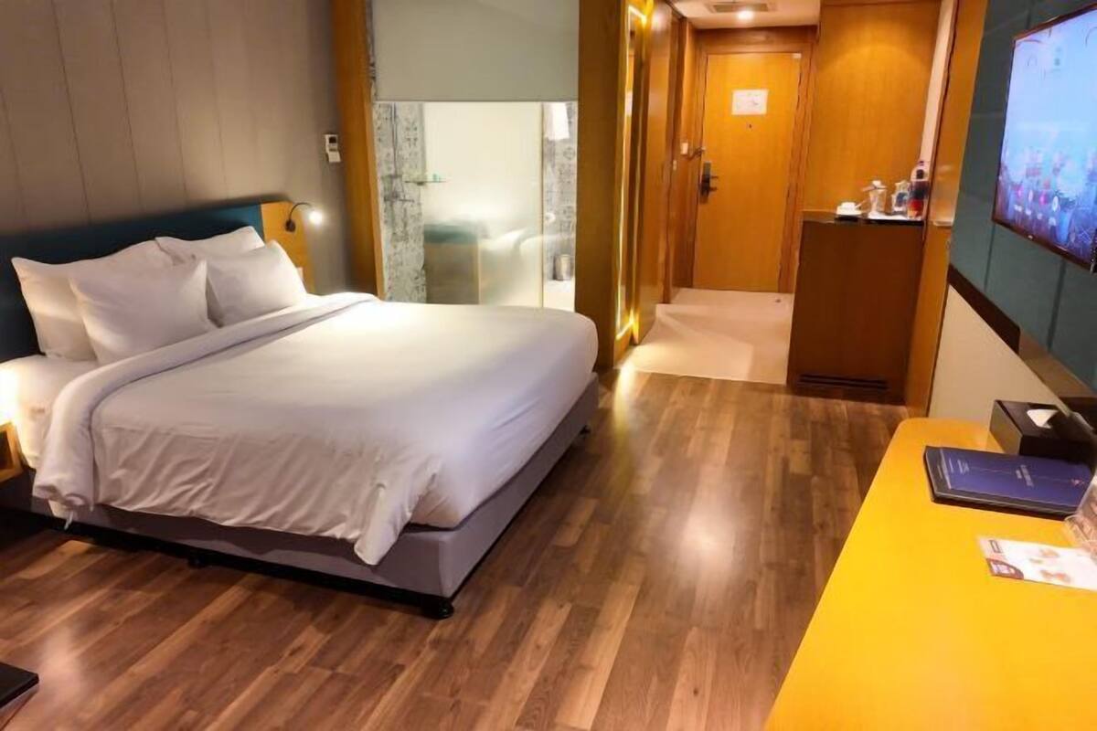 Quarto de hotel com uma cama, mesa de cabeceira e escrivaninha com um computador.