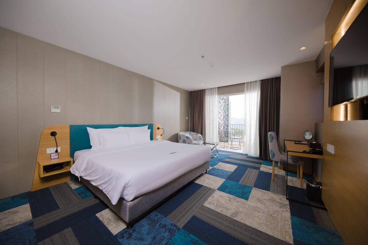 Quarto de hotel com uma cama grande, uma escrivaninha, uma cadeira e vista para o exterior.