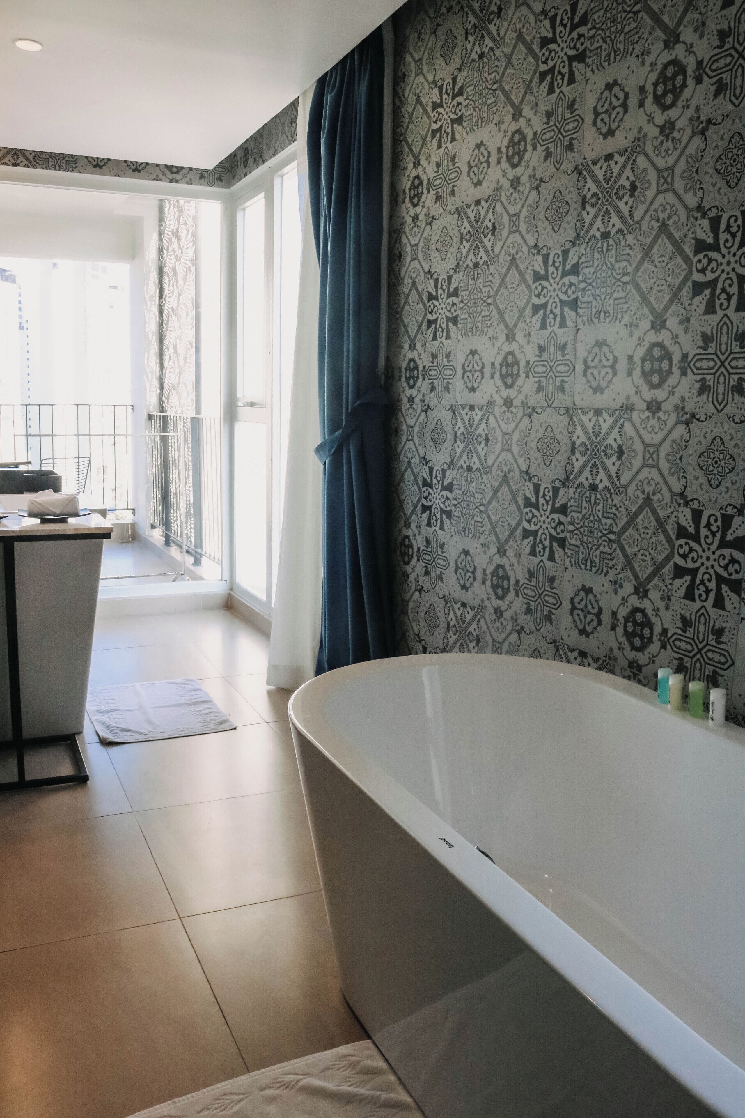 Un baño moderno con una bañera independiente, papel tapiz estampado y vistas a un balcón con barandilla.