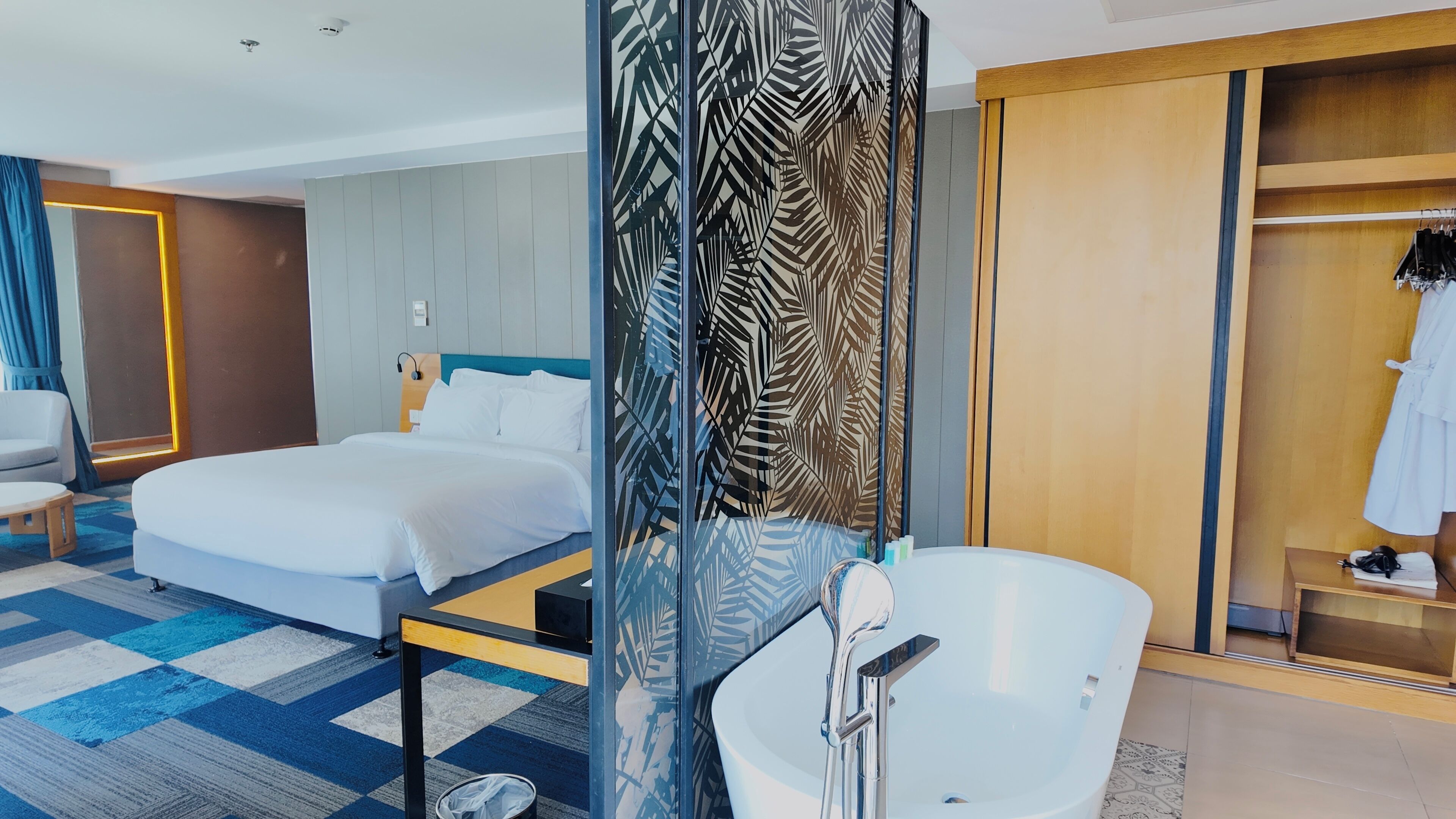 A hotel room with a bed, a desk, a chair, a bathroom with a bathtub, and a wardrobe.