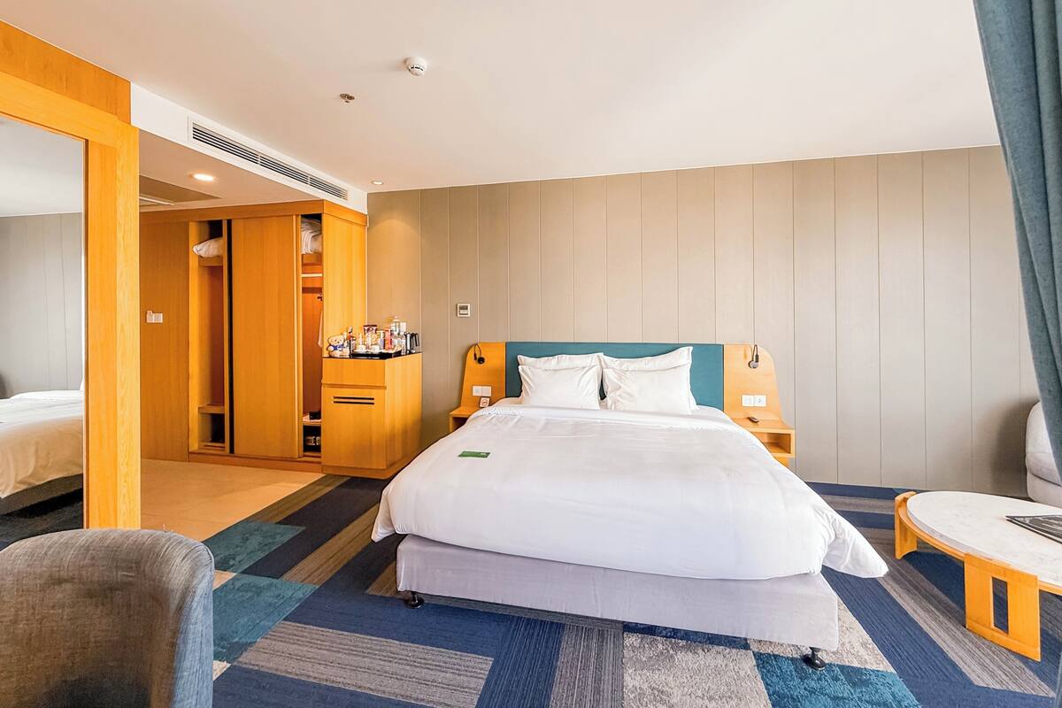 Quarto de hotel com cama, mesas de cabeceira, guarda-roupa e um pequeno espaço de estar.