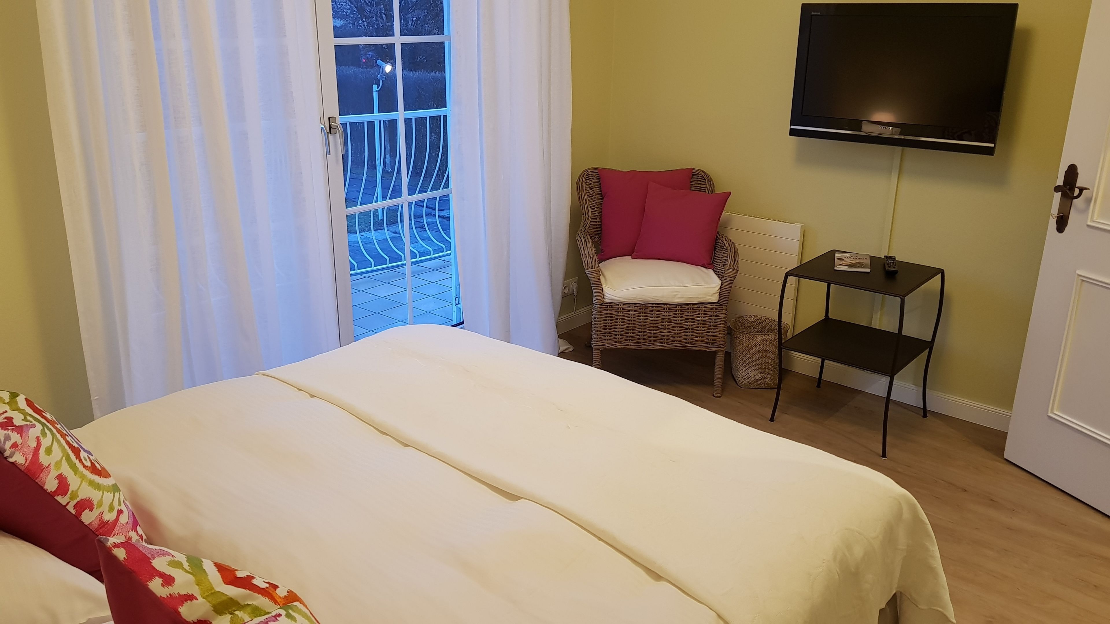 Una habitación con cama, una silla, una mesita y un televisor montado en la pared.