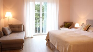 Un dormitorio con cama, sofá, sillón, lámpara y ventana con cortinas.