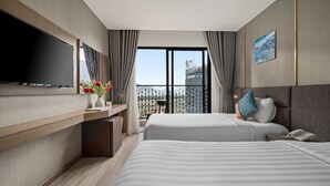 Habitación de hotel con dos camas, televisión, escritorio y balcón con vista a un edificio.