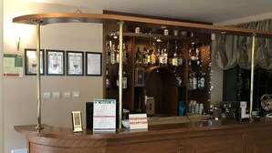 Un comptoir d’accueil en bois, avec une enseigne indiquant « réception », des certificats encadrés accrochés au mur, et une variété de bouteilles et de verres disposés sur des étagères derrière le comptoir.