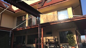 Un bâtiment à deux étages, doté d’un toit recouvert de tuiles rouges, de grandes fenêtres et d’un patio abrité avec un banc et des plantes en pot.