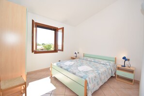 A bedroom with a bed, a nightstand, a chair, a window, and a wardrobe.