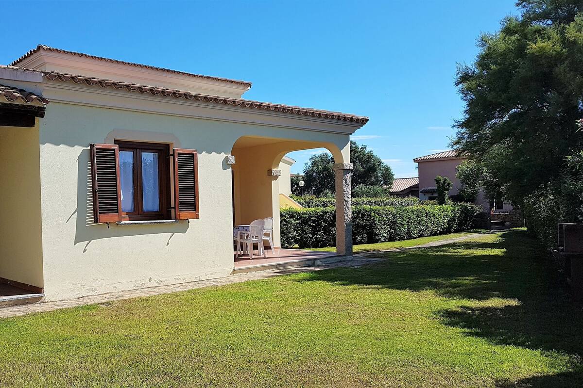 A single-story house with a tiled roof, a small porch with a table and chairs, and a well-maintained lawn.