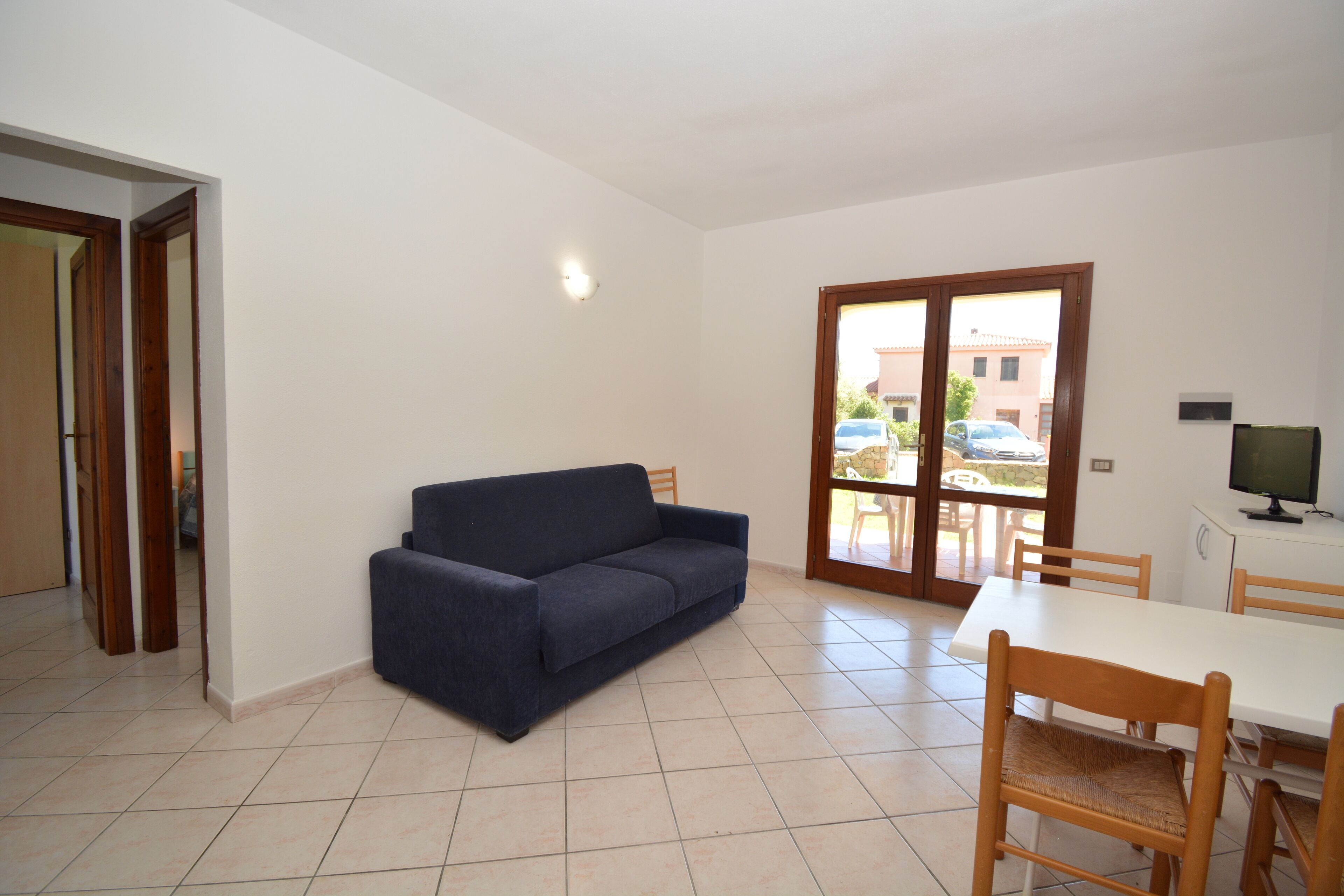 A living room with a sofa, a dining table with chairs, a TV, and a sliding glass door leading to an outdoor area.