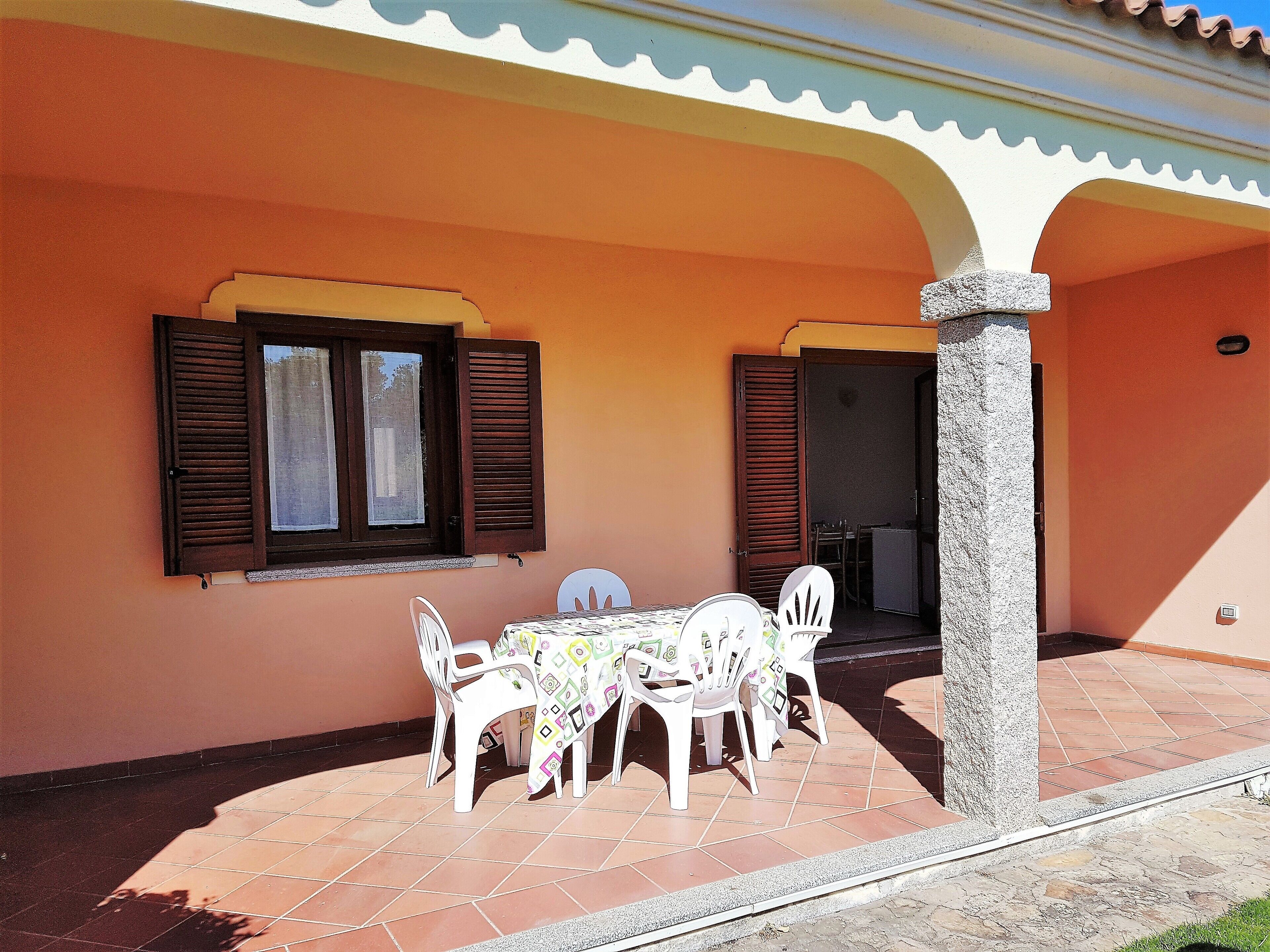 A patio with a table and chairs, a window with shutters, and a stone pillar.