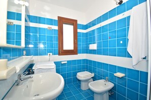A bathroom with blue tiles, a wooden-framed mirror, two sinks, a toilet, and a towel rack.