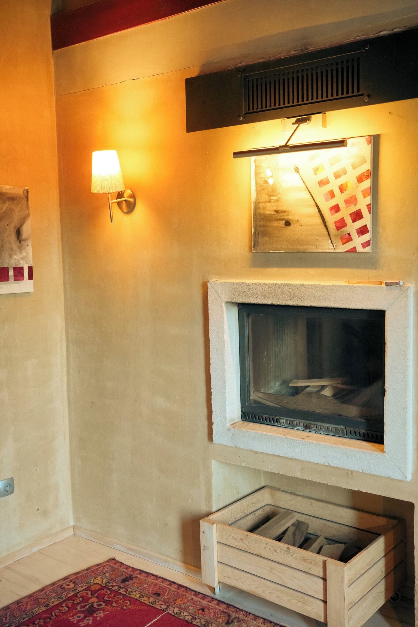 Una habitación con chimenea, una lámpara de pared, un tapete estampado y un baúl de madera.