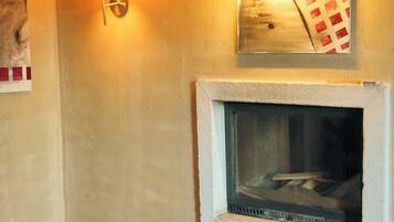 Una habitación con chimenea, una lámpara de pared, un tapete estampado y un baúl de madera.