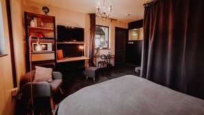 Habitación de hotel con una cama grande, un escritorio con silla, un televisor y una araña.