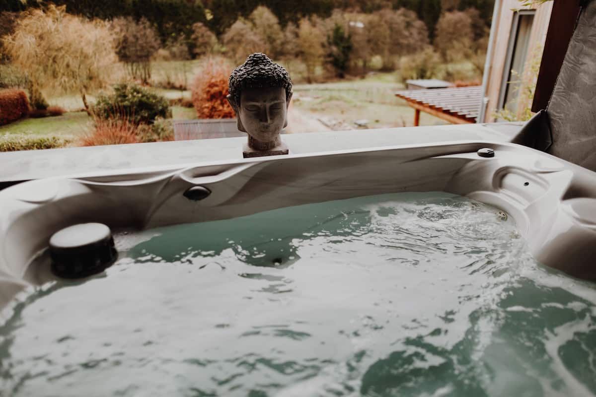 A hot tub with a Buddha statue in the background, surrounded by a garden.