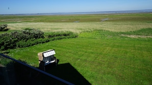 A view of a grassy field with a chair and a small structure, likely a gazebo, in the foreground. - Ferienwohnung Feskerdam 28 OG (Sylt)