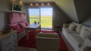 A modern living room with a large window, a flat-screen TV, a red sofa, a white sofa, and a small table. - Ferienwohnung Feskerdam 28 OG (Sylt)