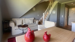 A living room with a sofa, a wooden table, and a staircase. - Ferienwohnung Feskerdam 28 OG (Sylt)