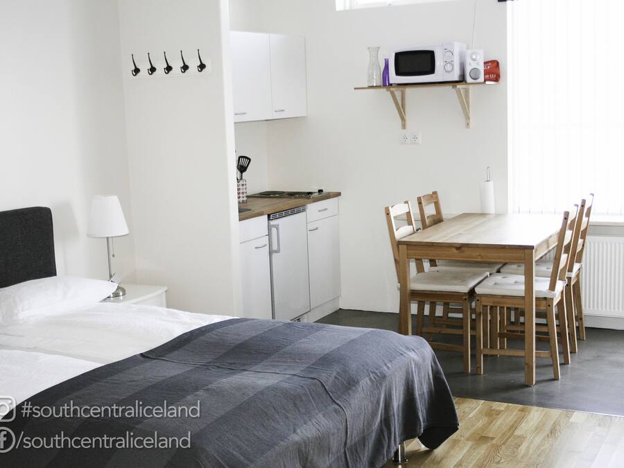 A bedroom with a bed, bedside table, lamp, and a small kitchenette with a microwave and toaster.