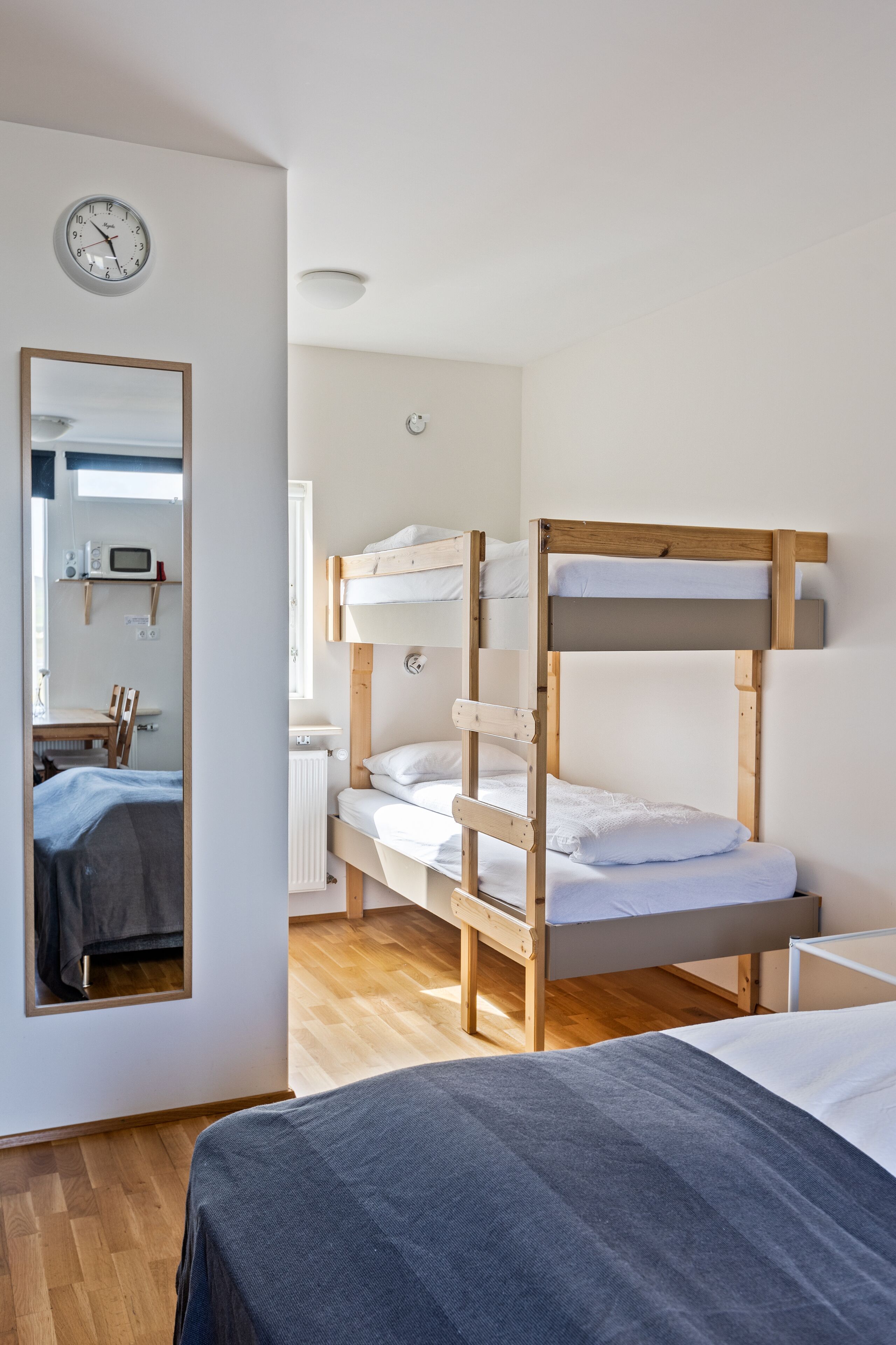 Quarto com beliches de madeira, um espelho, um relógio e uma pequena mesa com cadeira.