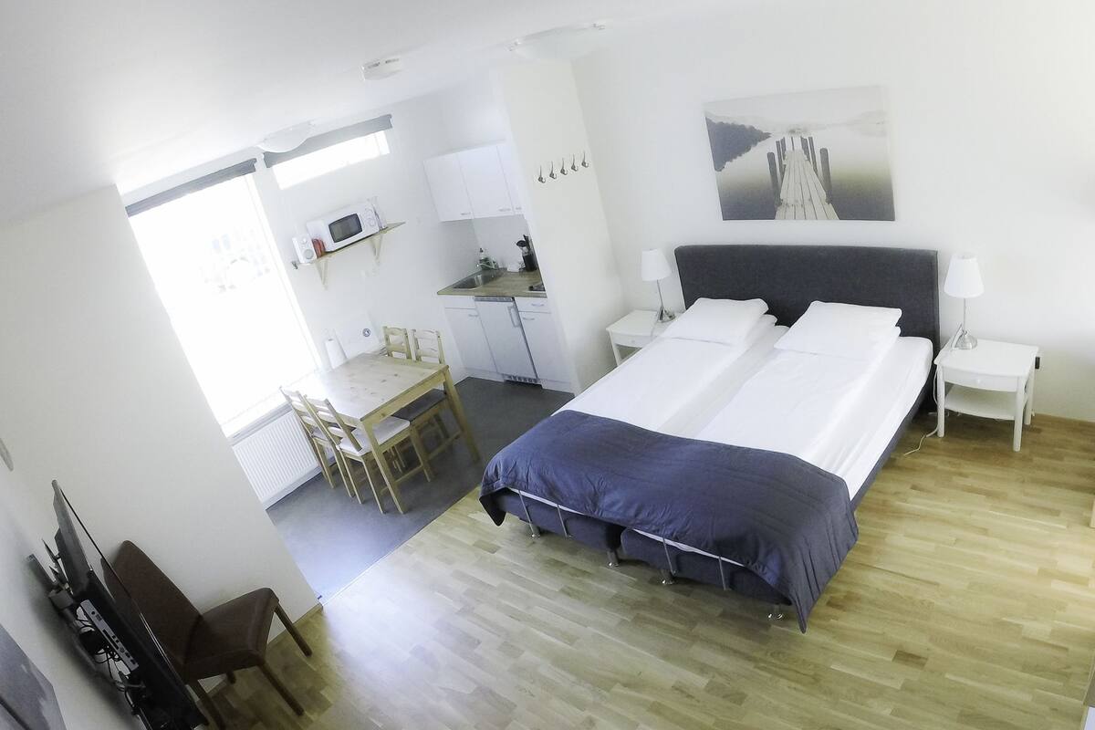 A modern hotel room with a large bed, a desk with a chair, a microwave, and a dining area.