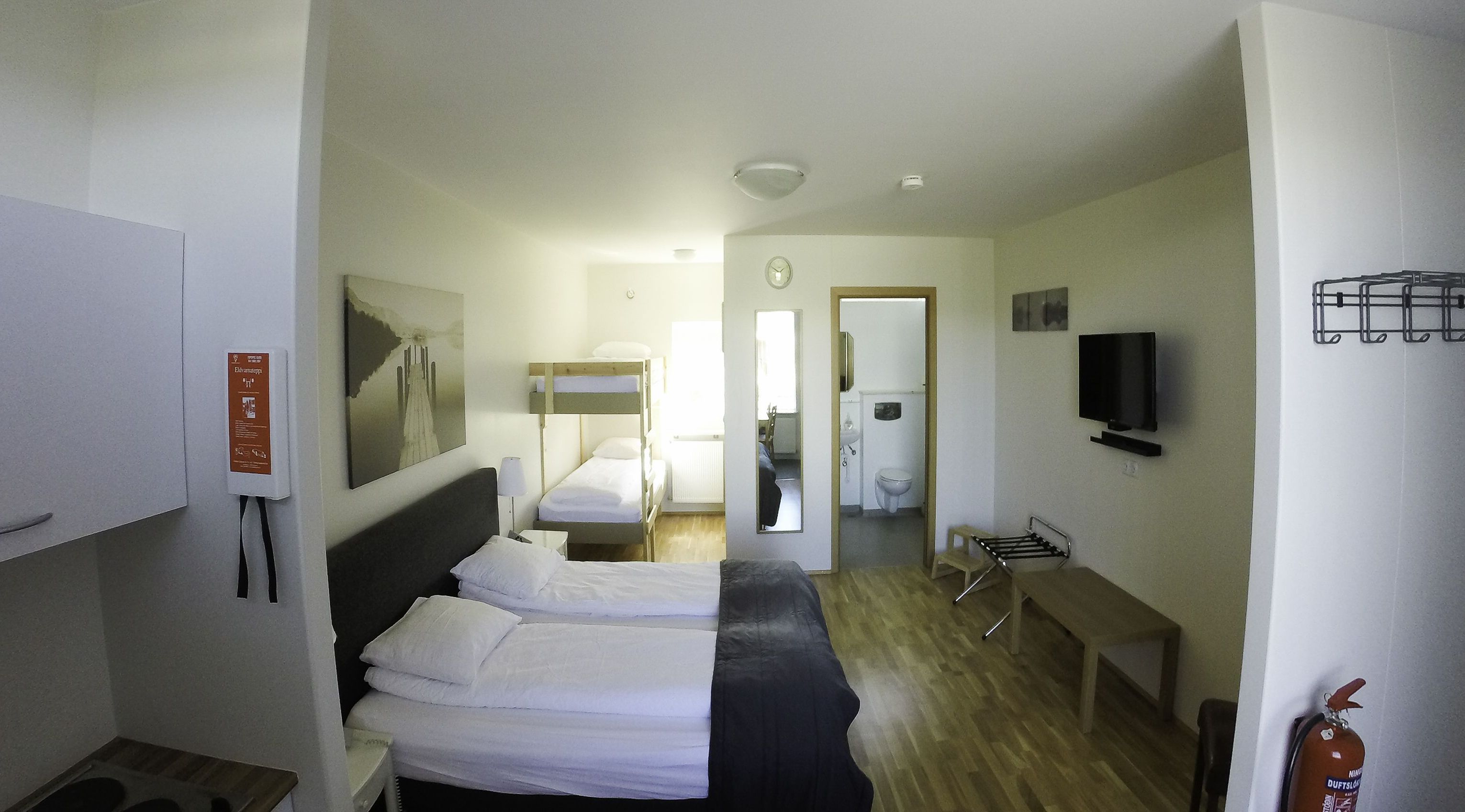 A hotel room with two beds, a TV, a mirror, a wooden bench, and a fire extinguisher.