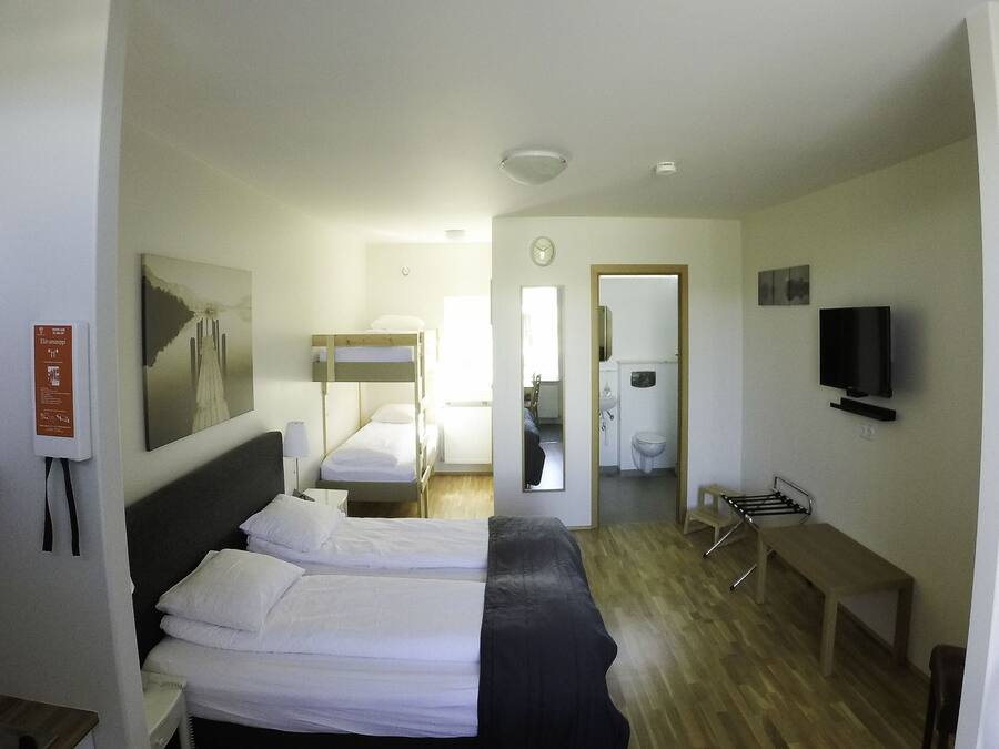 A hotel room with two beds, a TV, a mirror, a wooden bench, and a fire extinguisher.