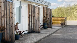 A row of cabins with wooden walls and a white door, each with a potted plant and a chair outside. - South Central Apartments (Selfoss)
