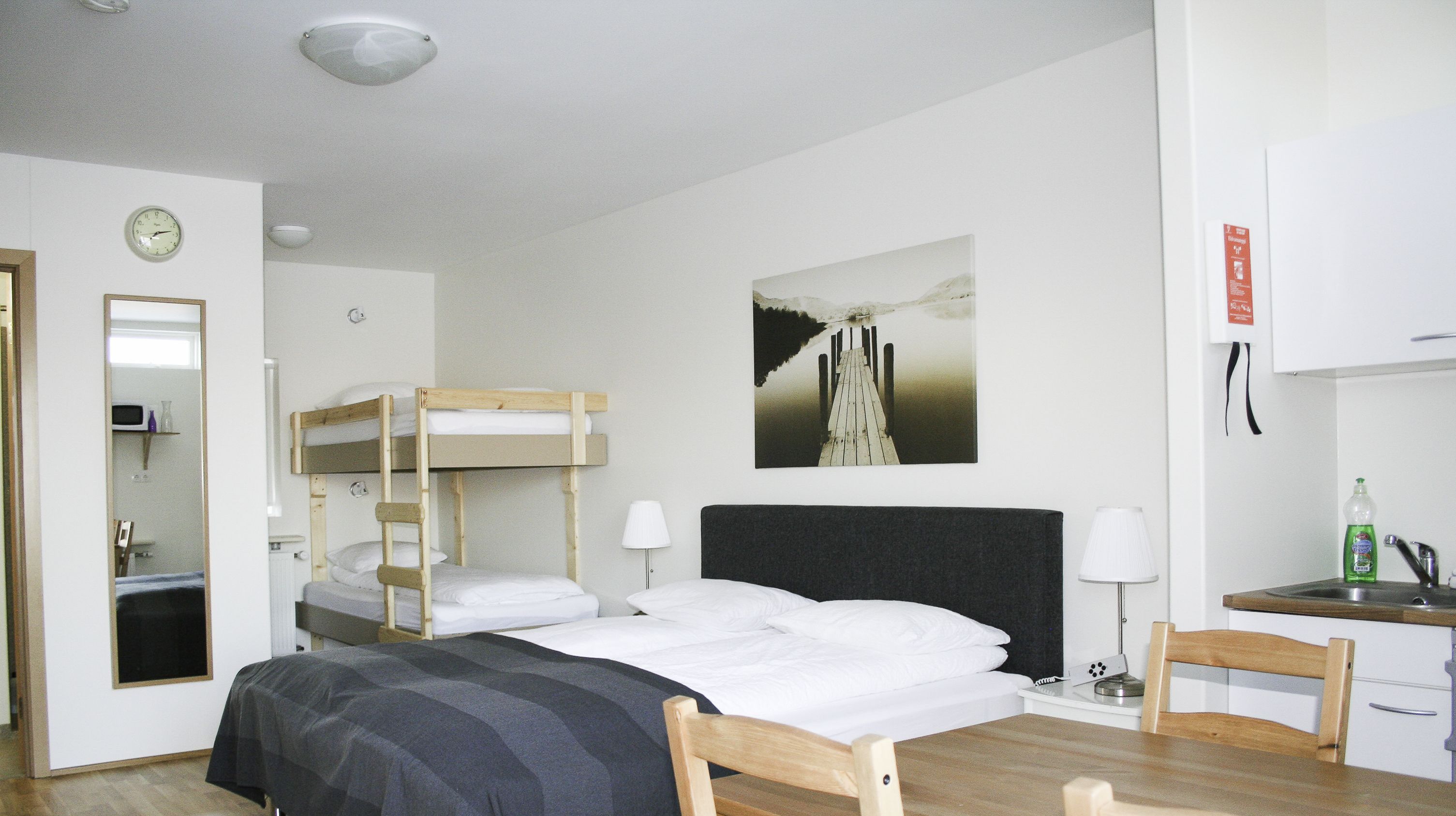 Ein Zimmer mit Stockbetten, einem Schreibtisch mit Stuhl, einem Spiegel, einer Uhr und einem Bild an der Wand.