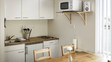 A compact kitchen with white cabinets, a wooden countertop, a microwave, a radio, and a dining table with chairs.