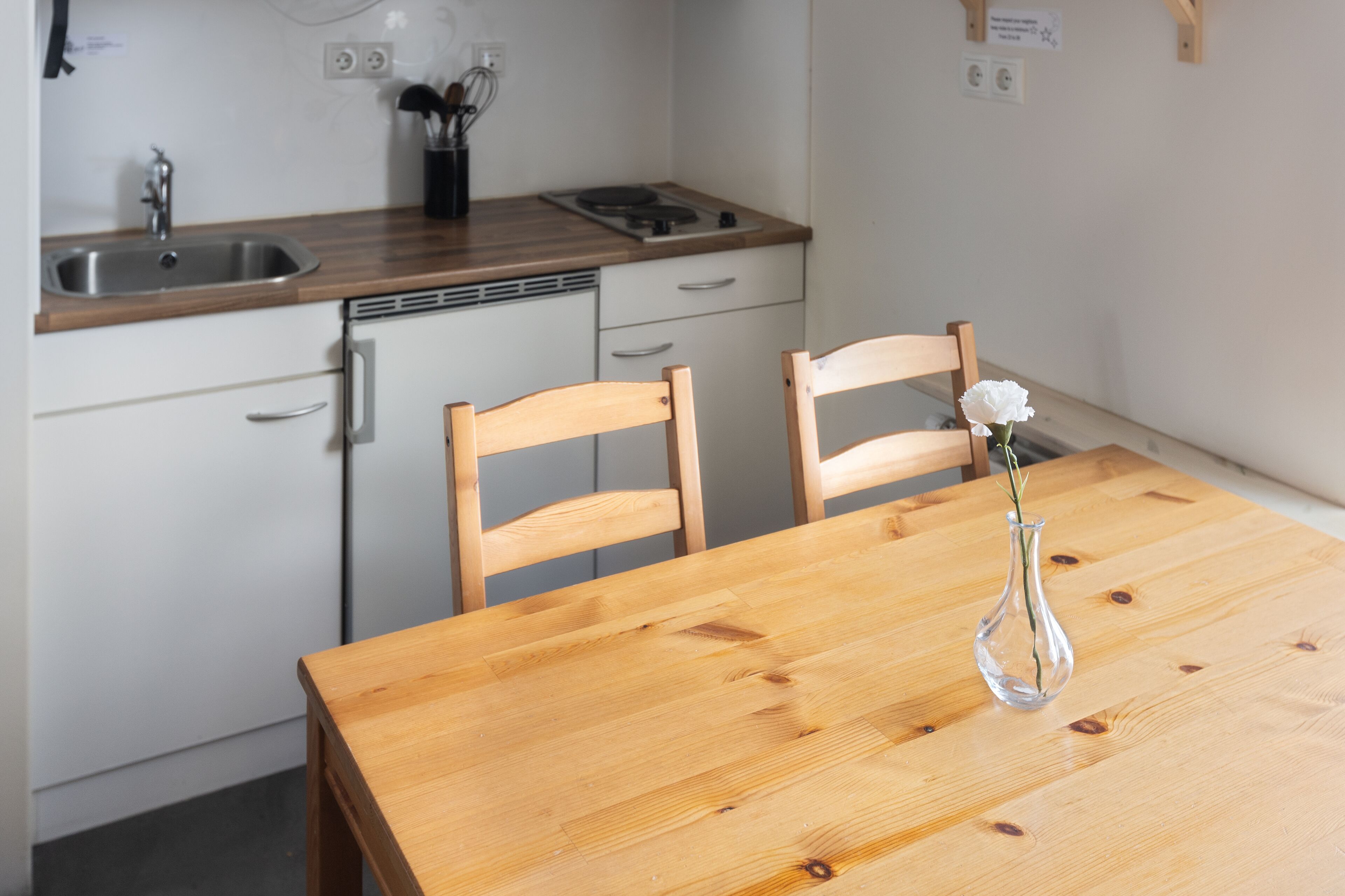 A kitchen with a wooden table, two chairs, a vase with flowers, a sink, and a stove.