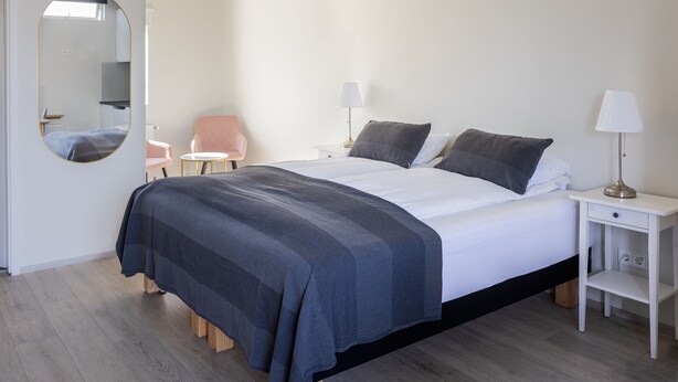 A bedroom with a bed, two bedside tables, a chair, a mirror, and a lamp. - South Central Apartments (Selfoss)