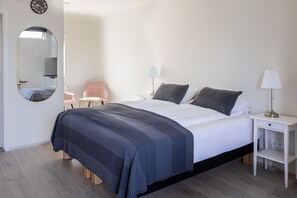 Un dormitorio con una cama, dos mesitas de noche, una silla, un espejo y una lámpara.